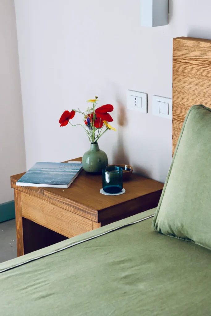 Luxurious room at La Segreta Country House in Menfi, Sicily, featuring a beautifully adorned bed with green satin bedding, a charming wooden side table with fresh flowers, perfect for an October luxury yoga retreat with the prestigious Planeta family.