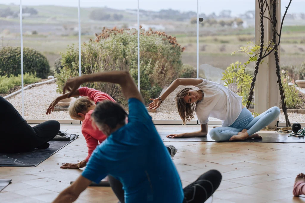 Sicily luxury yoga retreats a session of yoga participants doing side strechting view from the back, sicilian landscape in the background