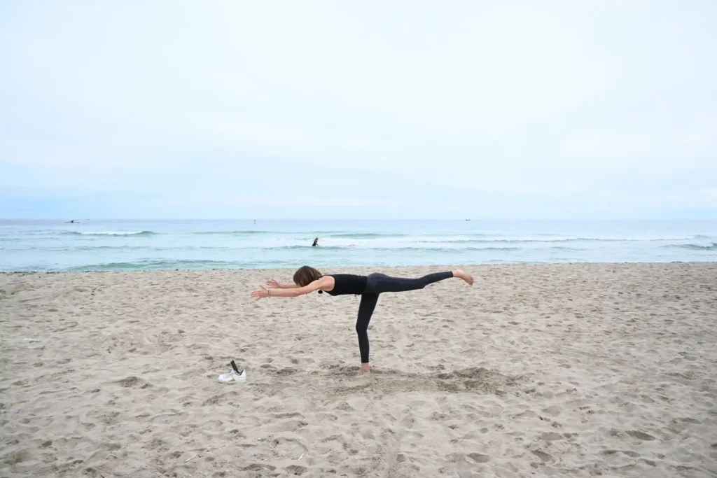 yoga trips on the beach, doing a perfect warrior one, withe ocean in the back